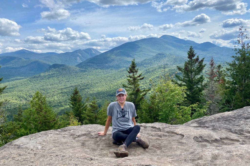 Female hiker sitting at top of Mt Jo in the Adirondacks with mountains in the background