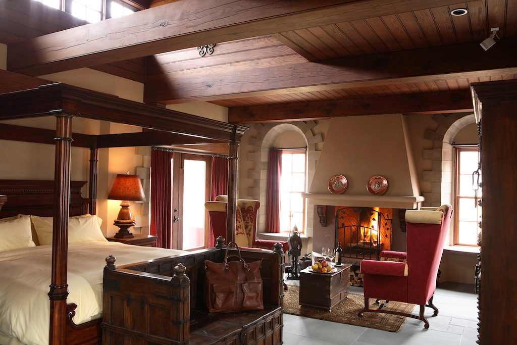 Bedroom in Winvian Farm with four poster bed and fireplace with two red chairs in the front