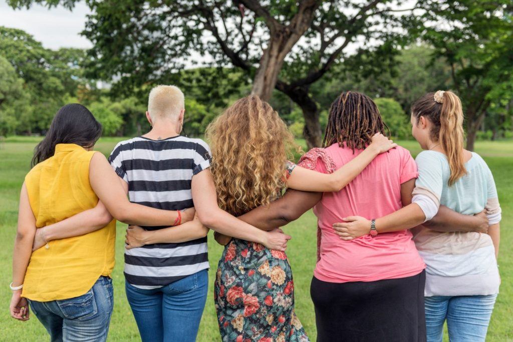 five women friends from behind with their arms around each other