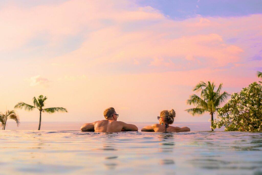 couple in an infinity pool looking out over sunset and palm trees