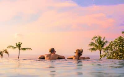 couple in an infinity pool looking out over sunset and palm trees