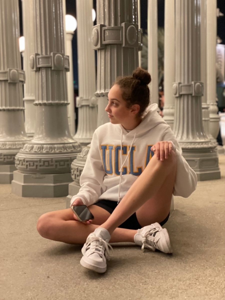 Girl in white UCLA sweatshirt sitting against white lampposts at LACMA exhibit