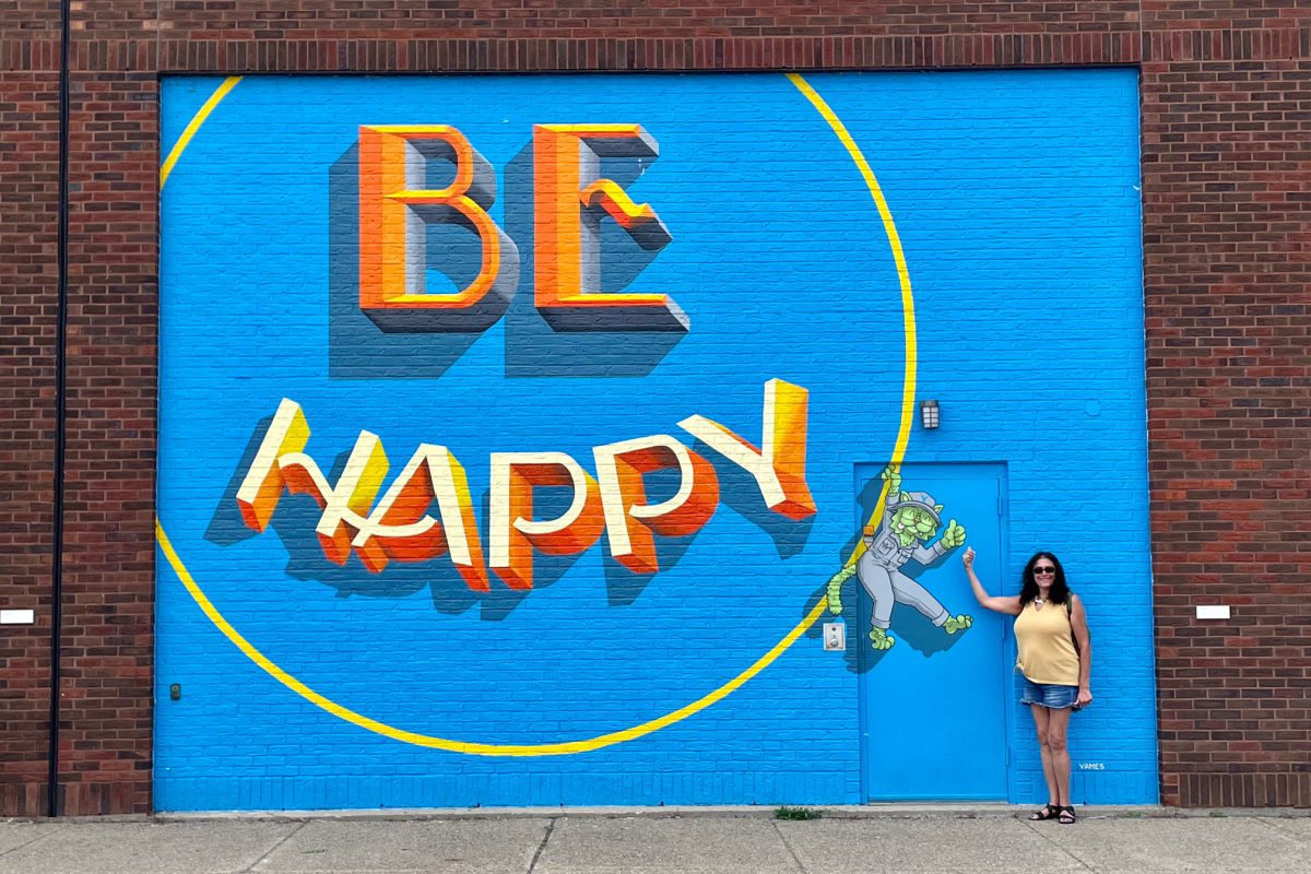 Woman in front of Be Happy mural in Buffalo