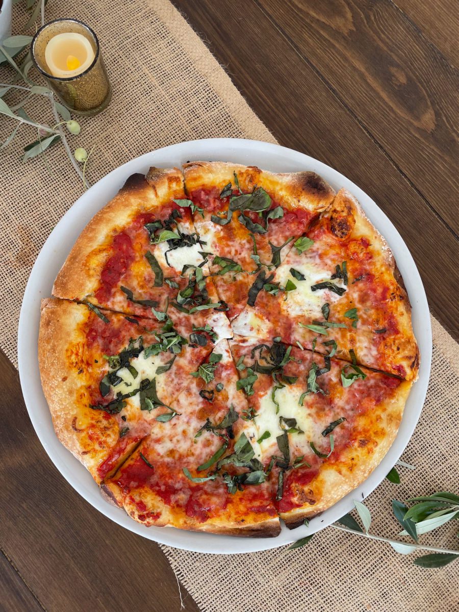 Pizza on a wood table with a candle and eucalyptus leaves at Queen Creek Olive Mill