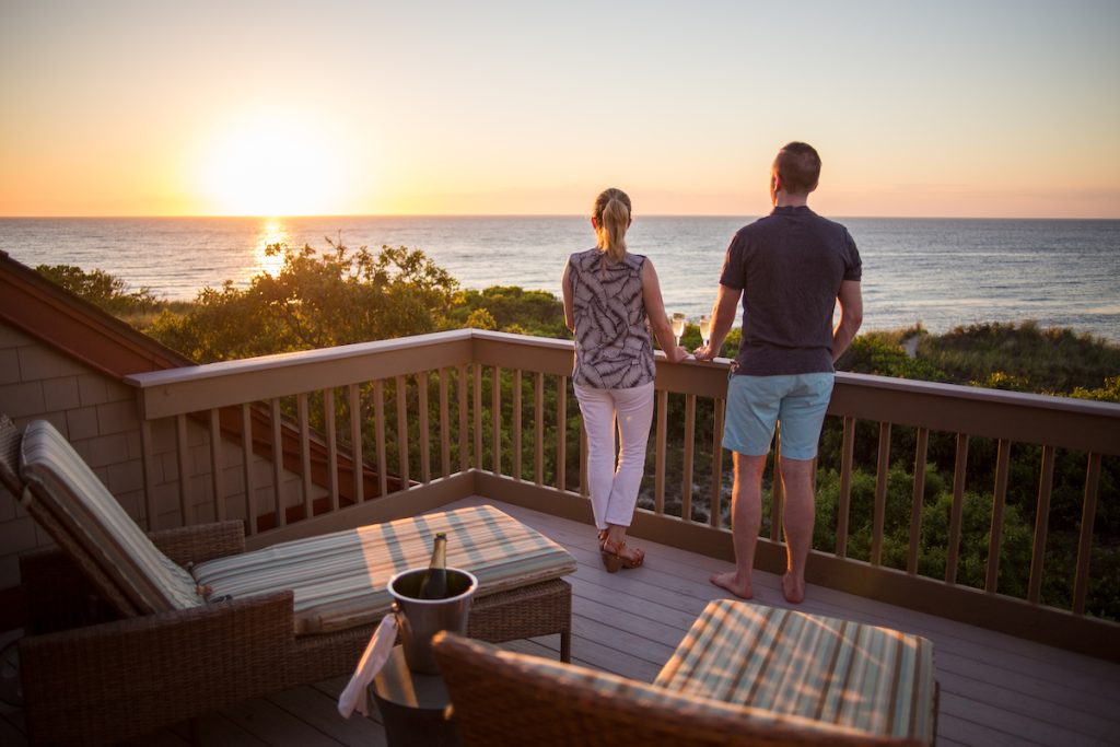 Couple with wine glasses looking at the sunset on the balcony at the Ocean Edge resort mansion