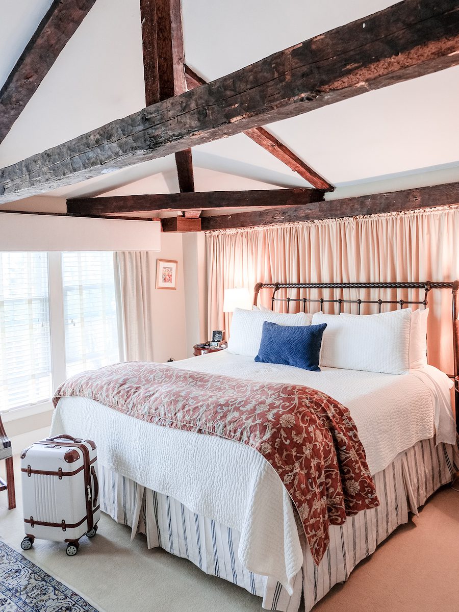 Room at the Harbor Light Inn with wood beam ceilings and white linens with peach curtains