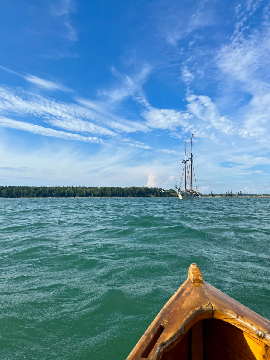 Schooner Heritage from the water with the tip of a wooden sailboat in the forefront