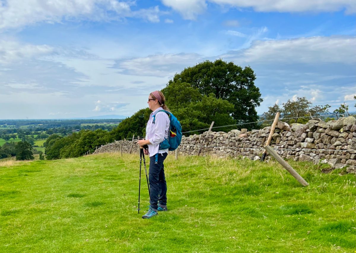 Female hiker with backpack and hiking poles next to Hadrian's Wall
