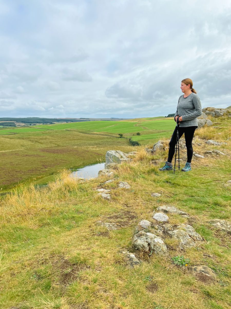 Female hiker in black tights and grey shirt holding hiking poles on a hillside