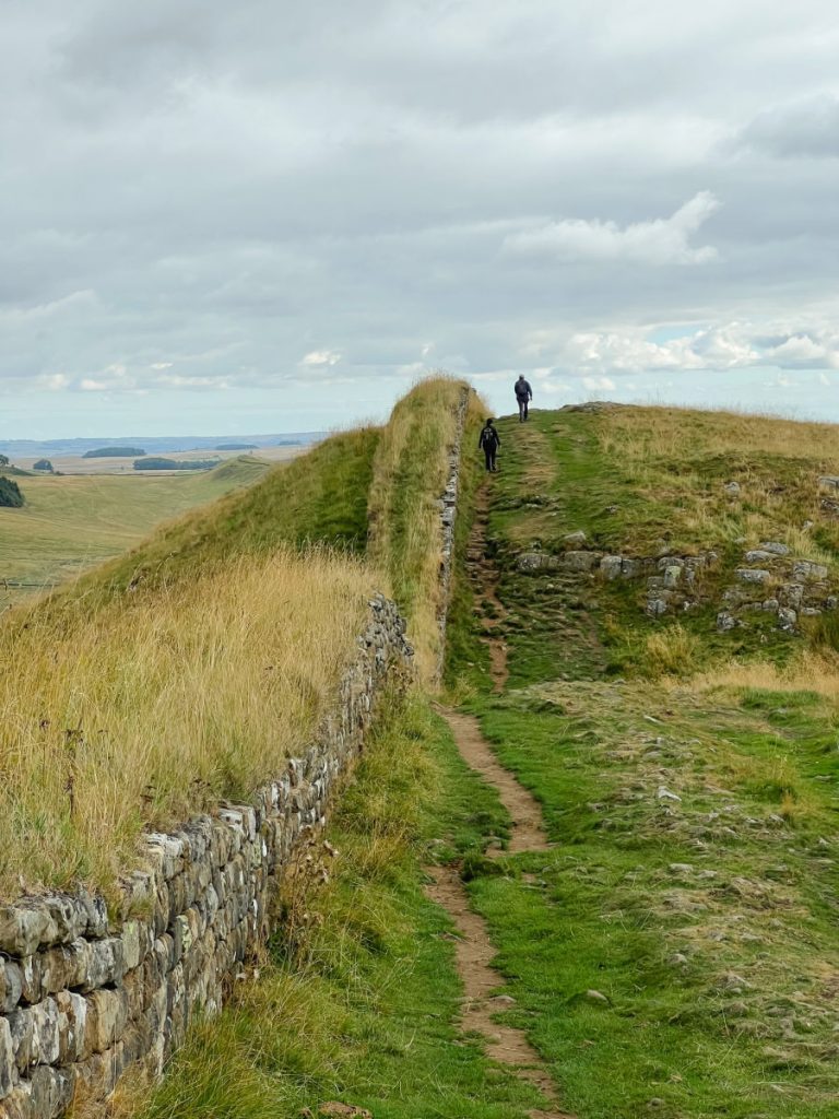 People walking up hill next to Hadrian's Wall
