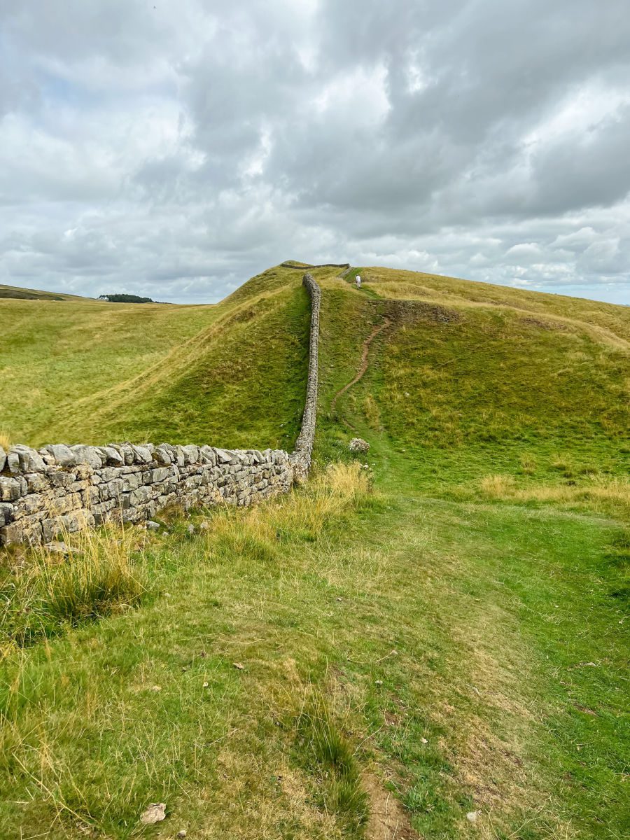 Person walking up hill by Hadrian's Wall in the distance