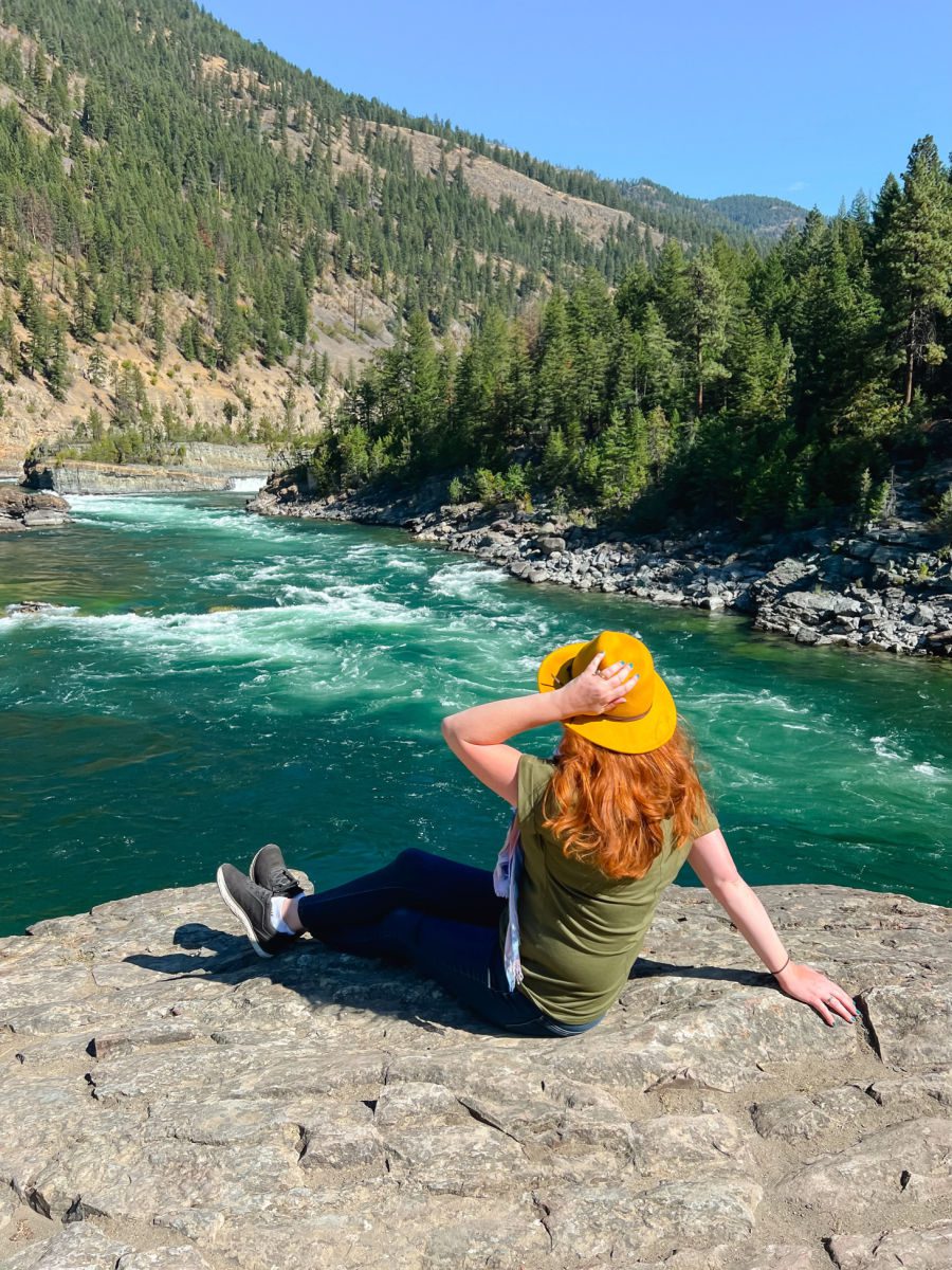 Keryn in a yellow hat from behind sitting in front of the Kootenai river