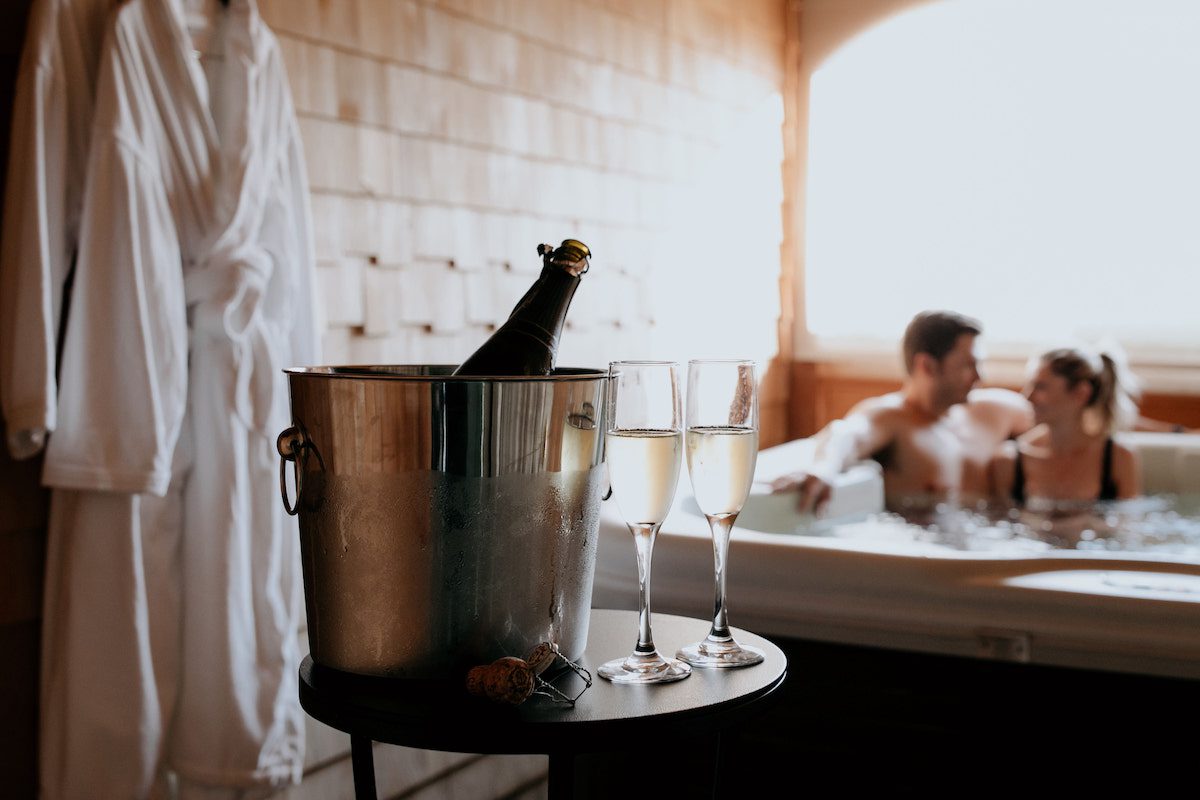 Champagne in bucket with flutes in front of couple in tub